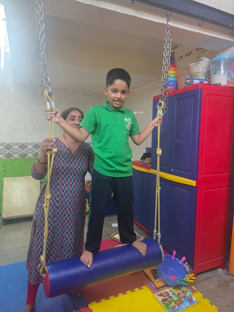 Student balancing on sensory bolster swing guided by teacher